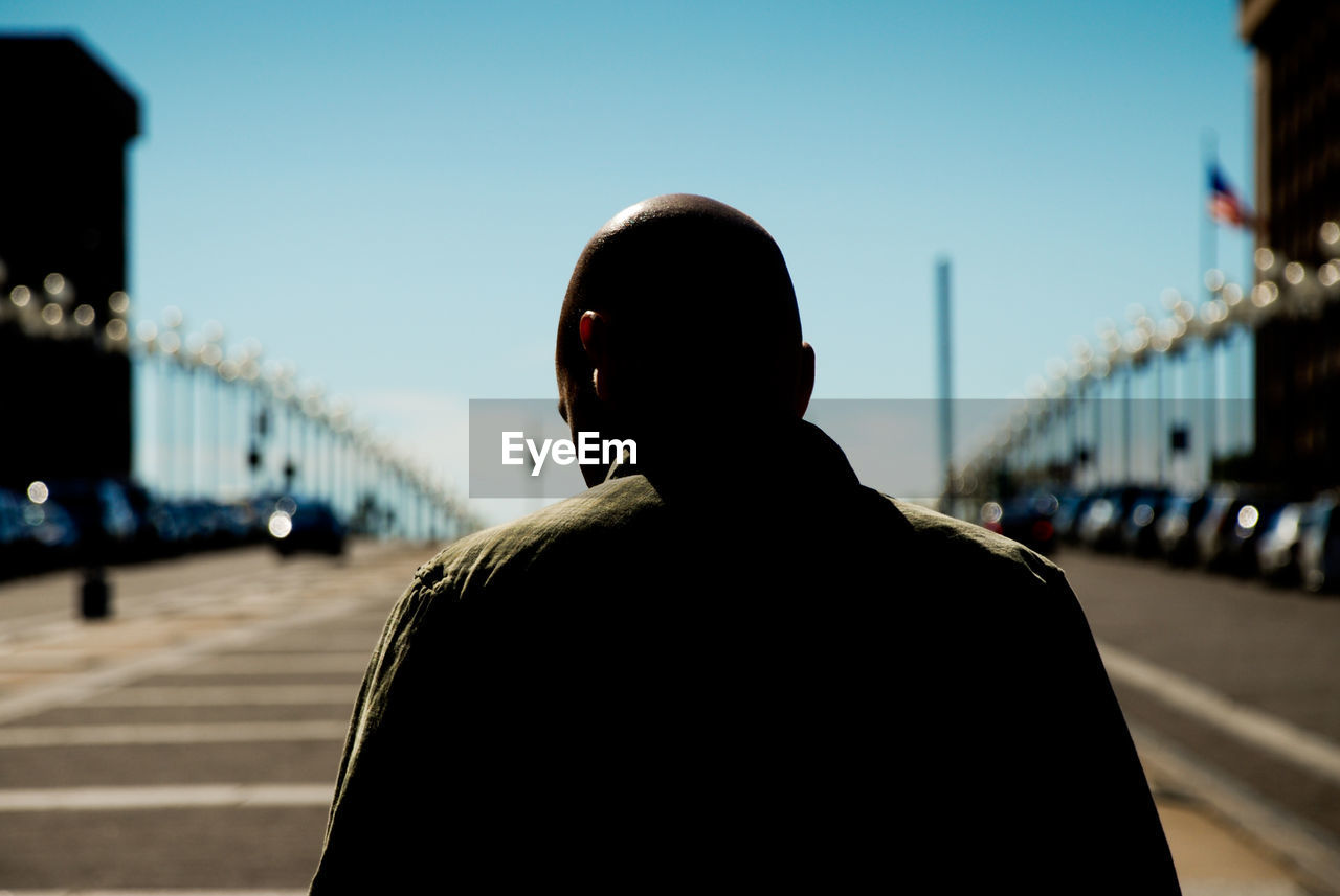 Rear view of man standing on bridge against sky in city