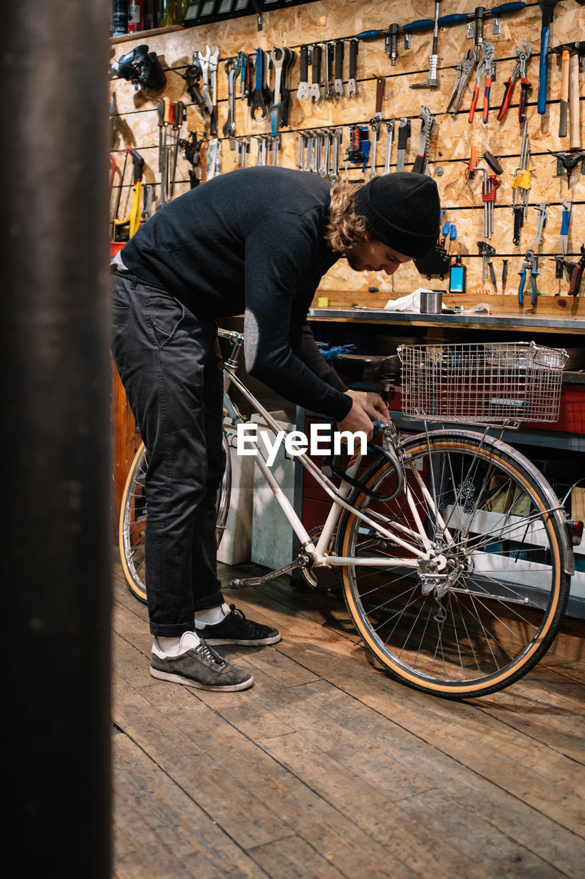 Side view of busy male master fixing bike while working in shabby repair workshop