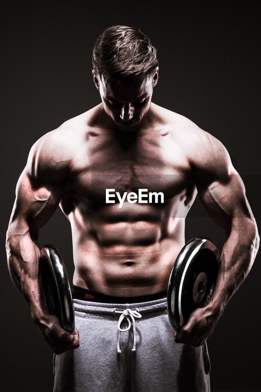 Shirtless muscular man exercising against black background