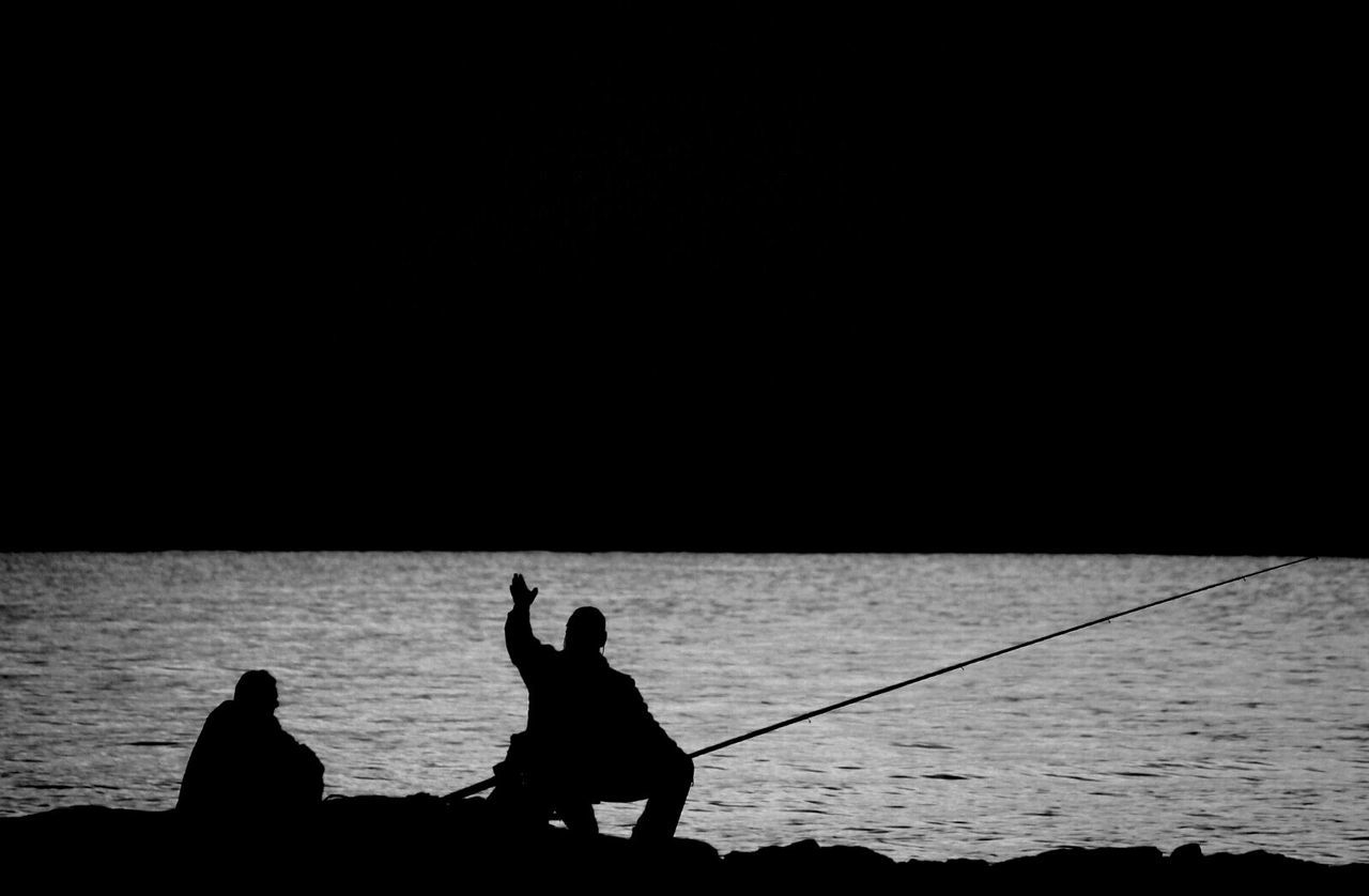 Silhouette person fishing at lakeshore