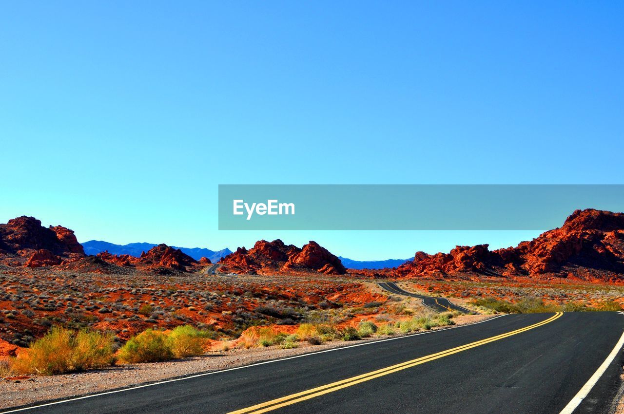 Country road leading towards mountains against blue sky