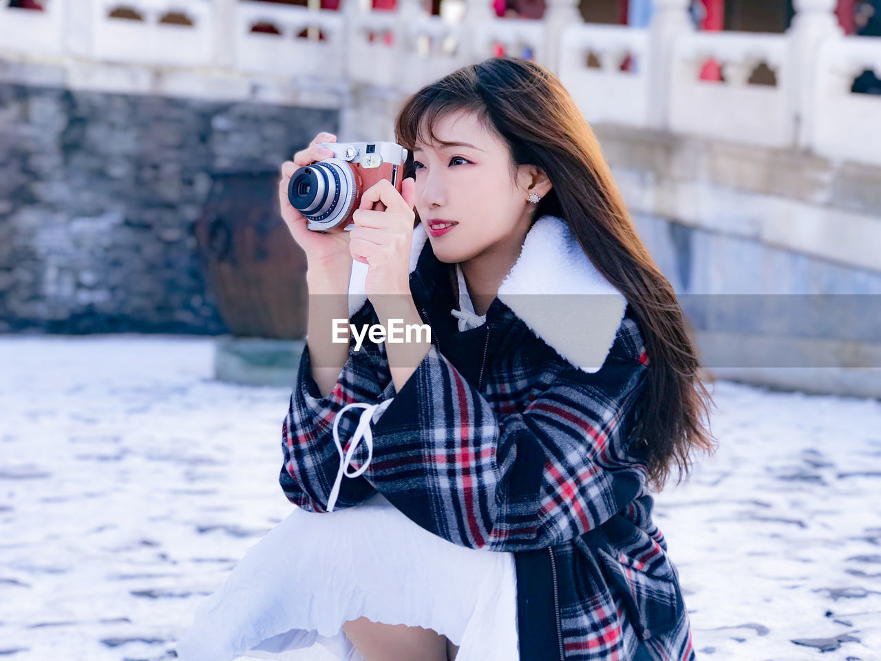 YOUNG WOMAN PHOTOGRAPHING WHILE HOLDING CAMERA