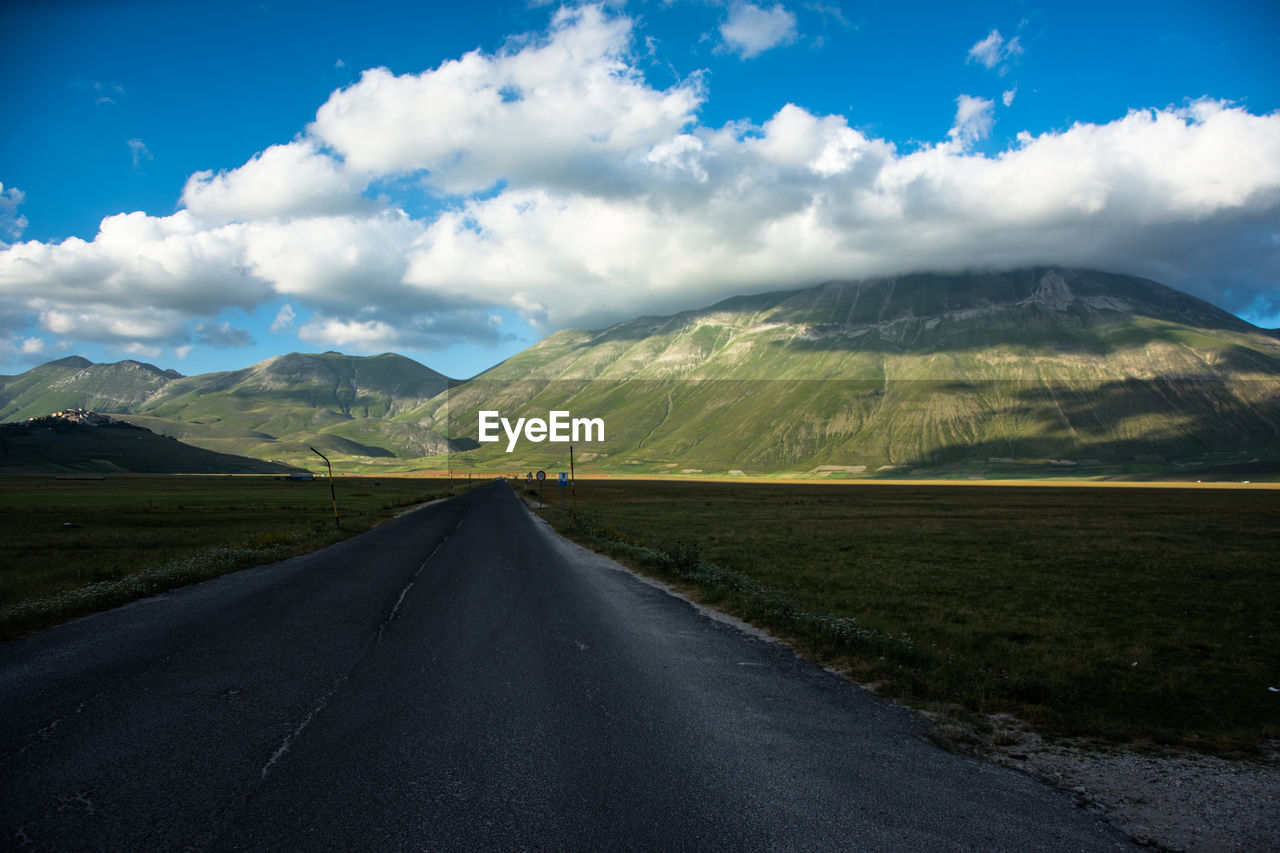 Empty road leading towards mountains against sky