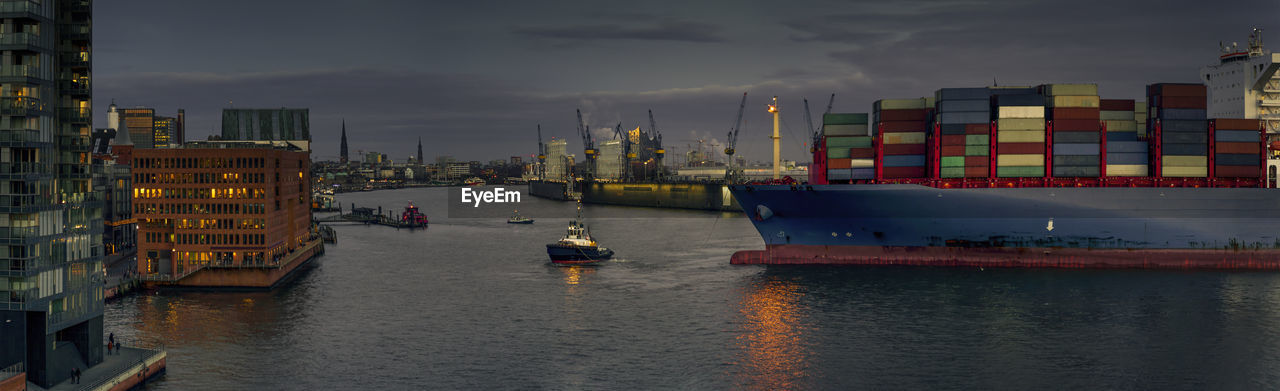 Boats on river by city against sky at dusk