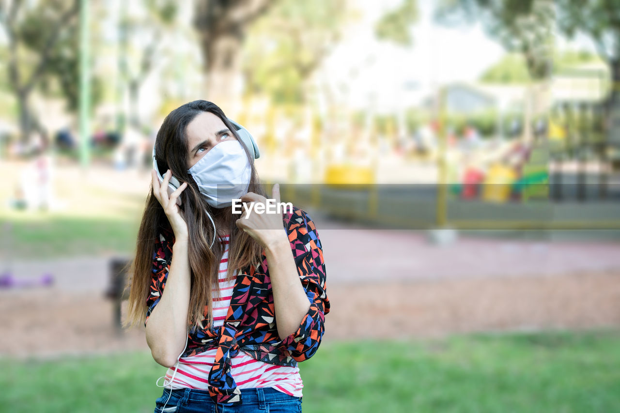 Woman wearing mask and headphones sitting at park