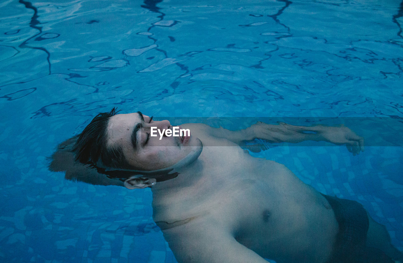 High angle view of shirtless man relaxing in swimming pool