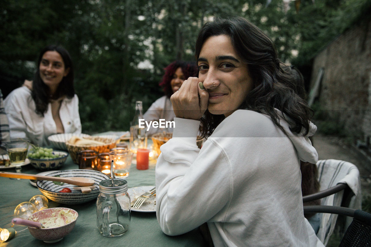 Portrait of smiling woman at dining table during dinner party in back yard