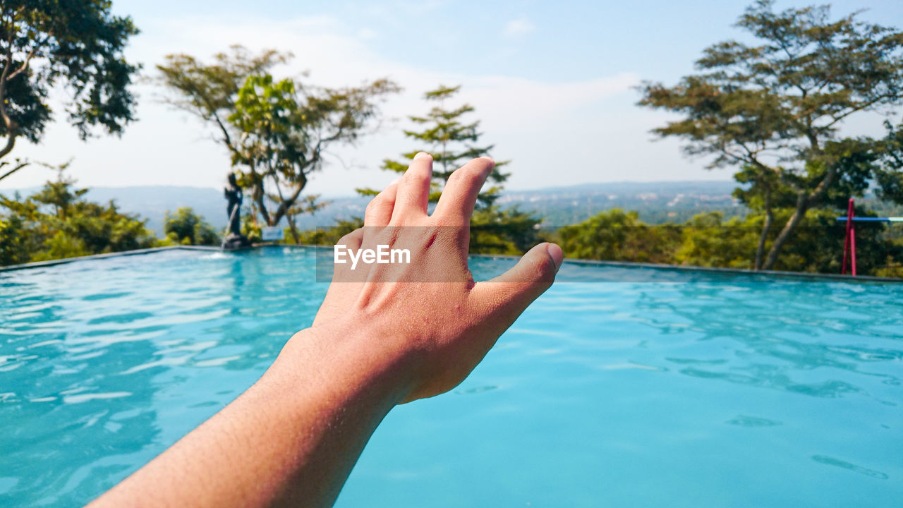 Cropped image of hand against swimming pool