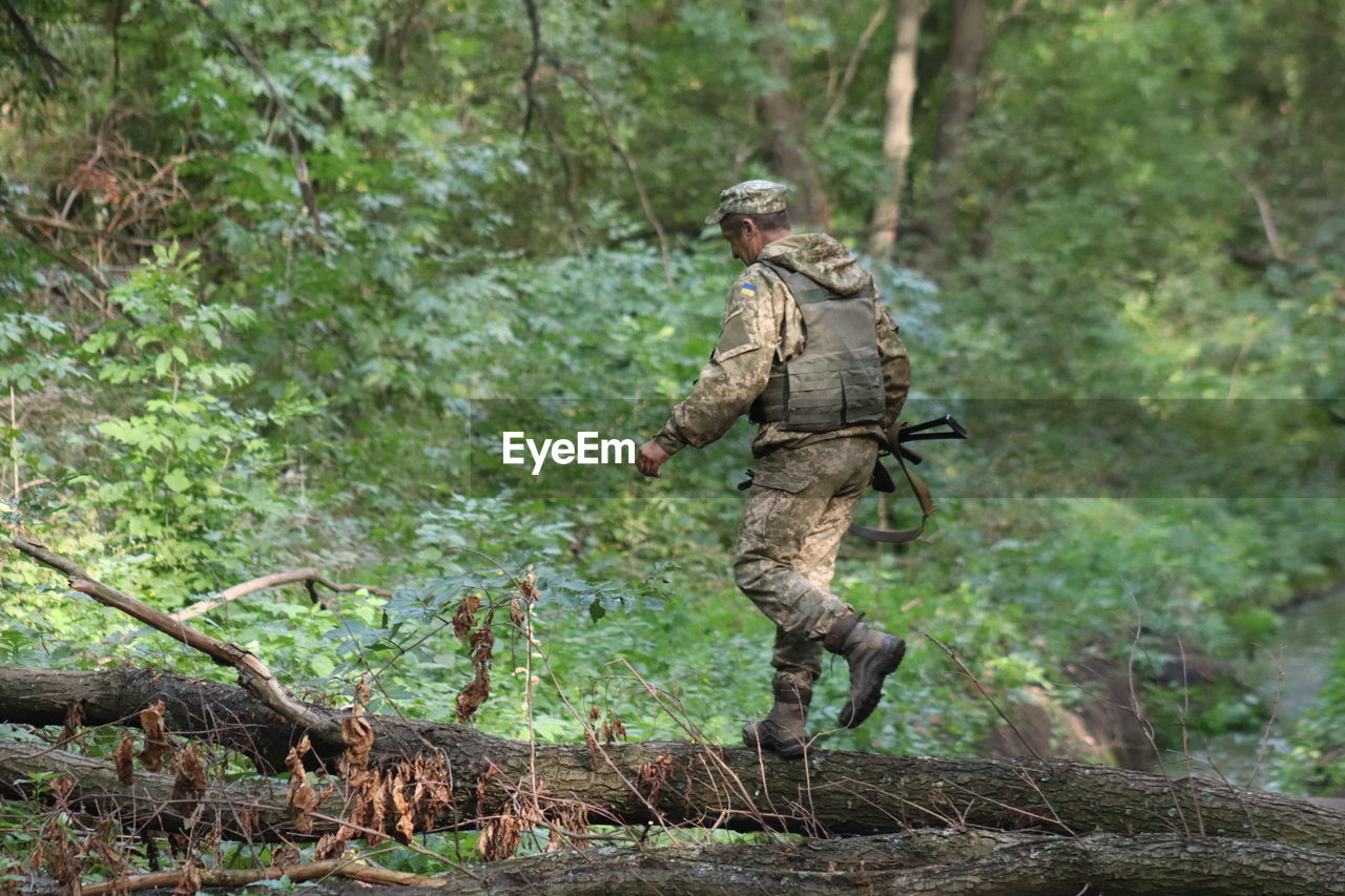 Army soldier walking on fallen tree in forest