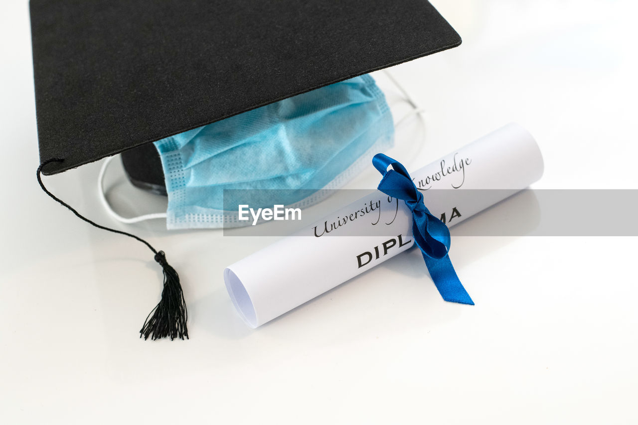 Closeup of graduation hat with degree and surgical mask on white background. virtual celebration