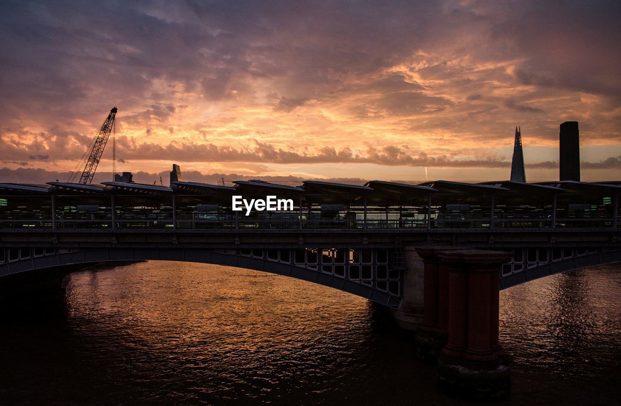 SILHOUETTE OF BRIDGE OVER RIVER AGAINST CLOUDY SKY