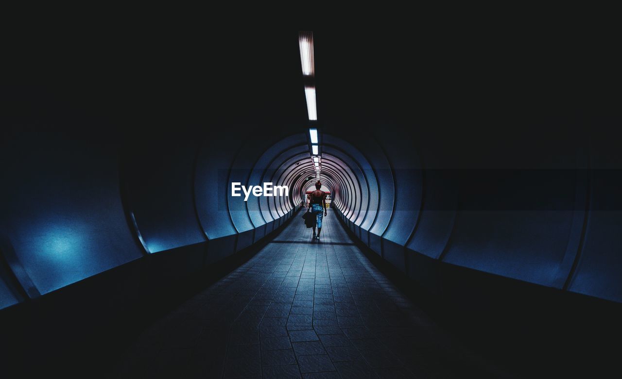 Rear view full length of woman walking in illuminated tunnel