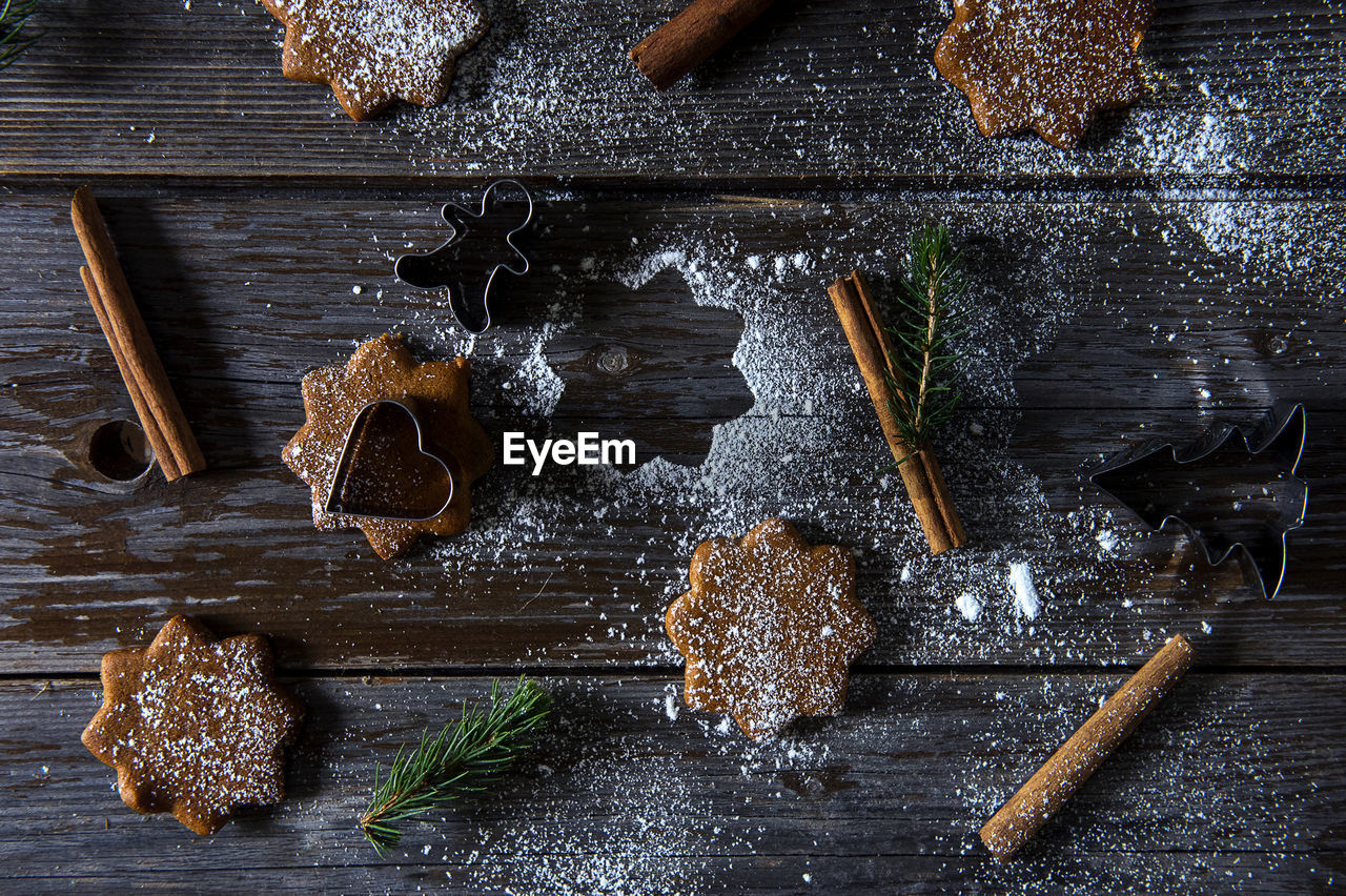 Directly above shot of powdered sugar over cookies and cinnamons on wooden table