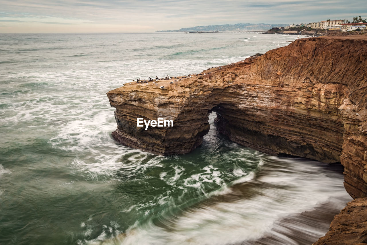 Long exposure surf crashing against beach bluffs on a cloudy day