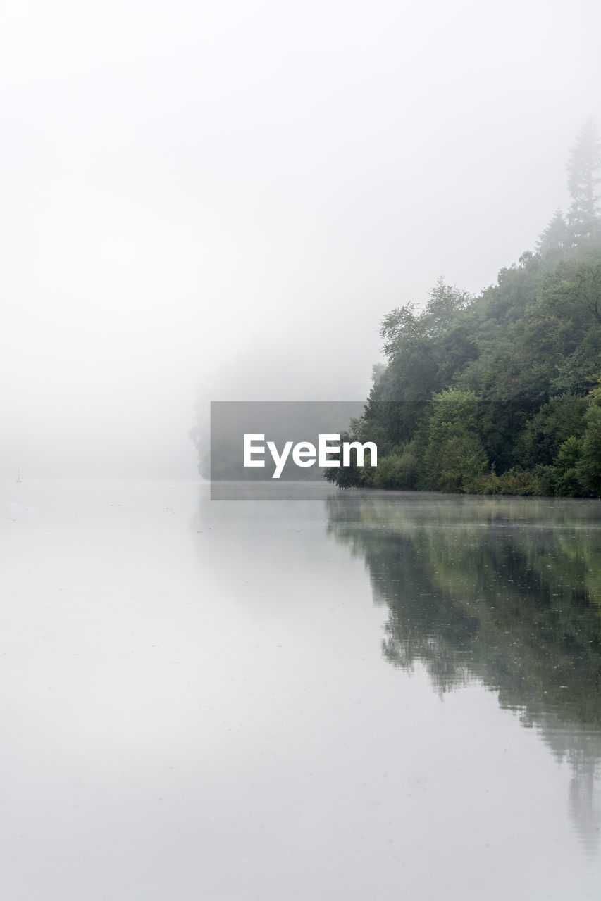 Reflection of trees in river against sky during foggy weather