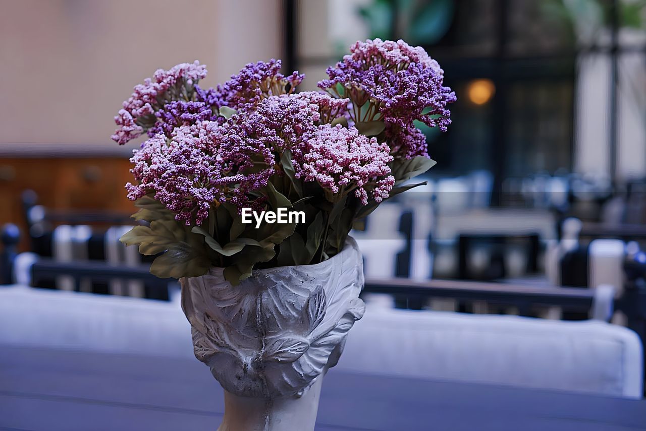 Greco-style vase/bust of a female head holding bouquet of purple flowers or lilacs. 