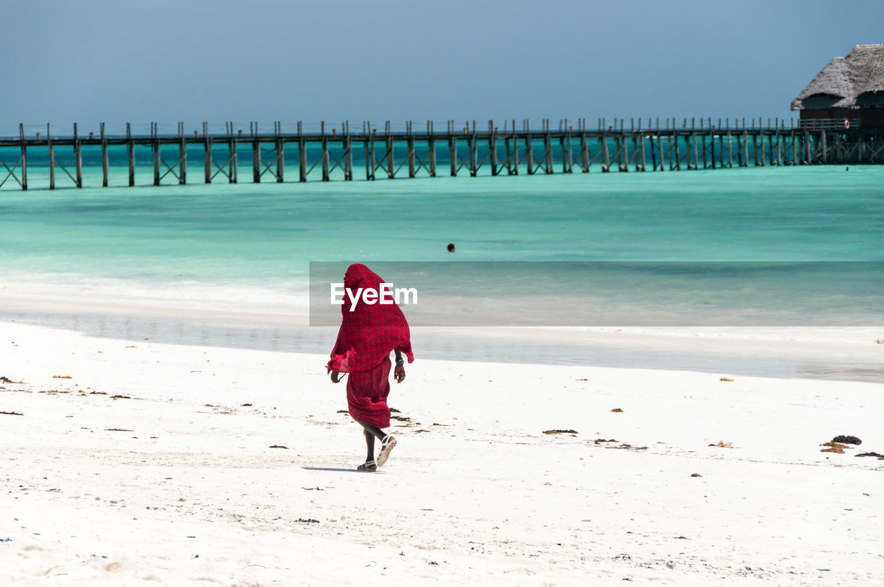 Rear view of masai warrior walking at beach against sky