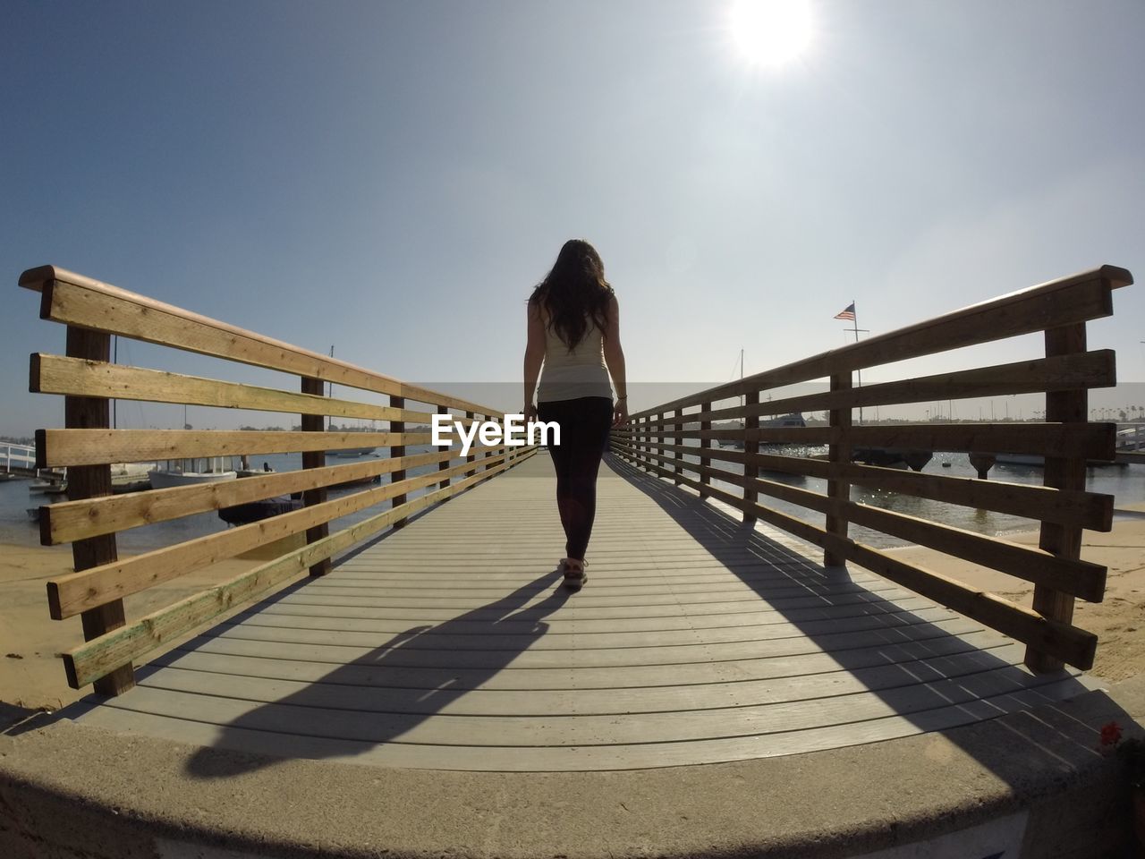 Rear view of woman standing on footbridge against sky