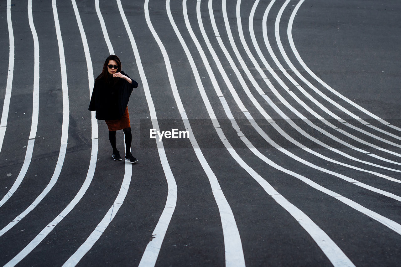 Full length portrait of young woman standing on striped asphalt