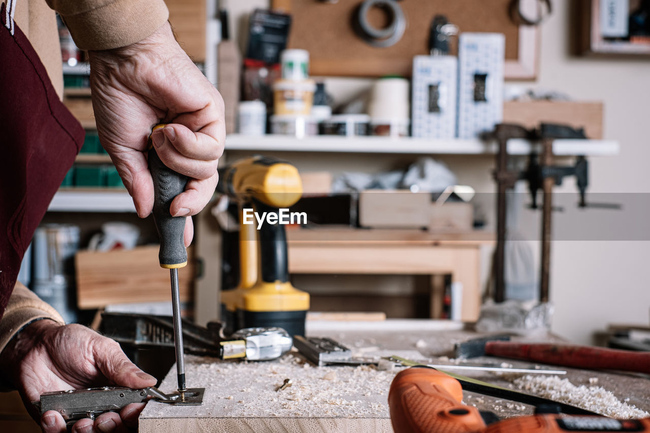 Midsection of carpenter tightening screw in workshop