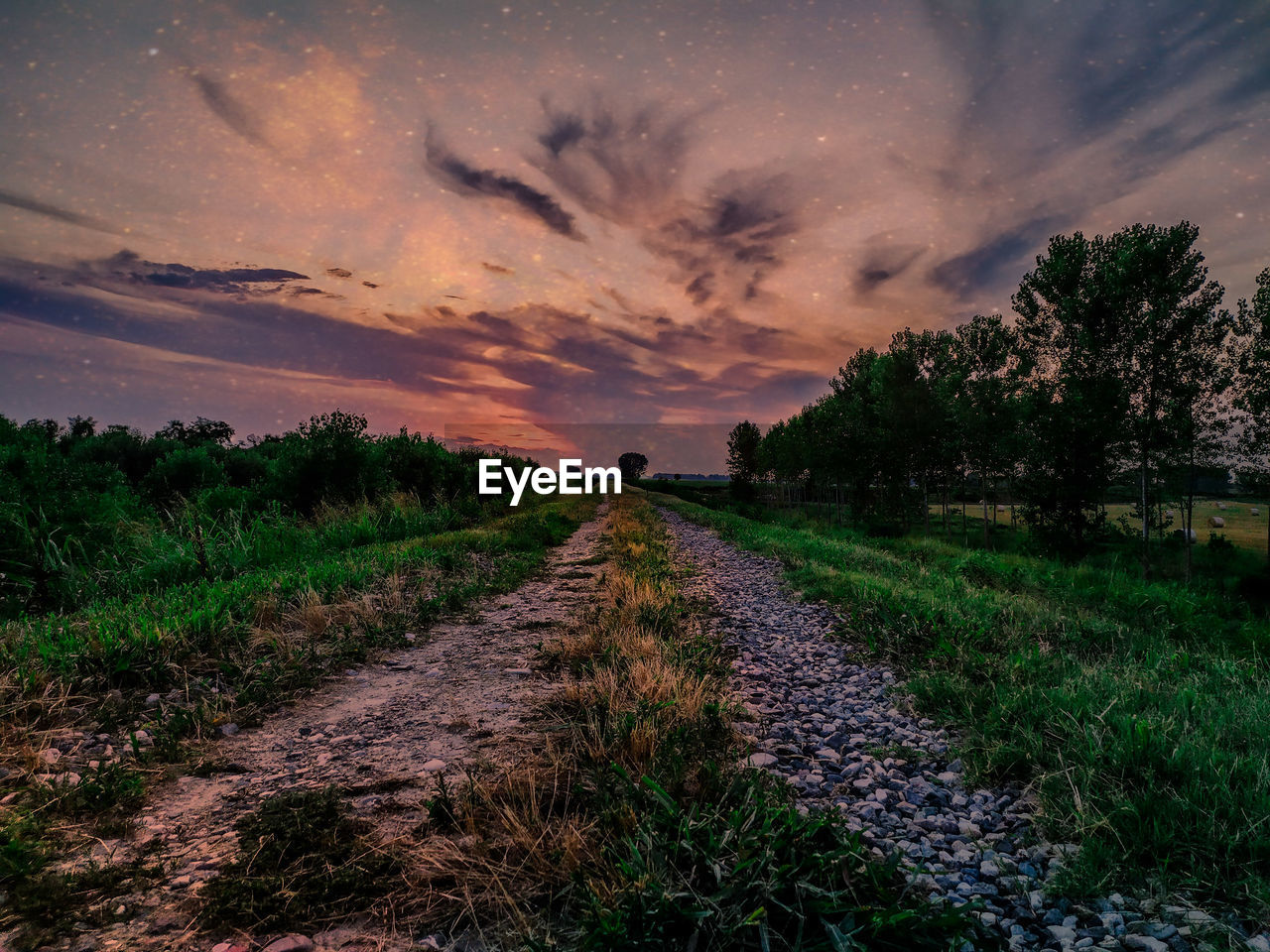 DIRT ROAD AMIDST FIELD AGAINST SKY DURING SUNSET