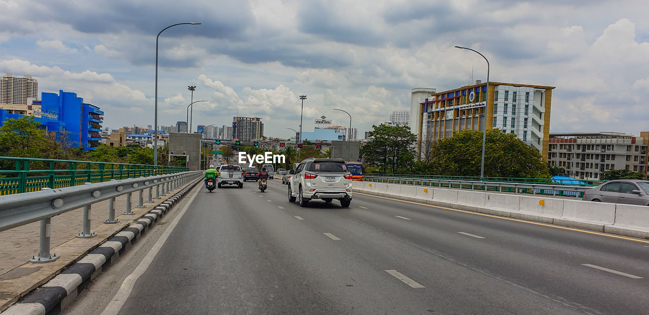 Cars on road by buildings in city against sky