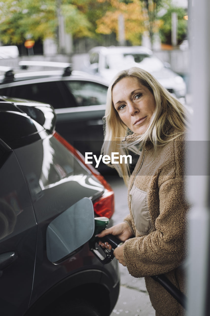 Mature woman with blond hair pumping gas in car at station