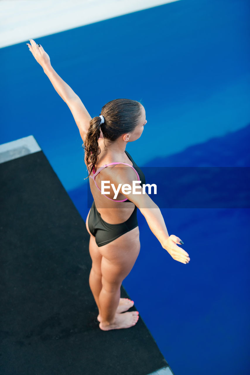 High angle view of mid adult woman standing on diving board over swimming pool