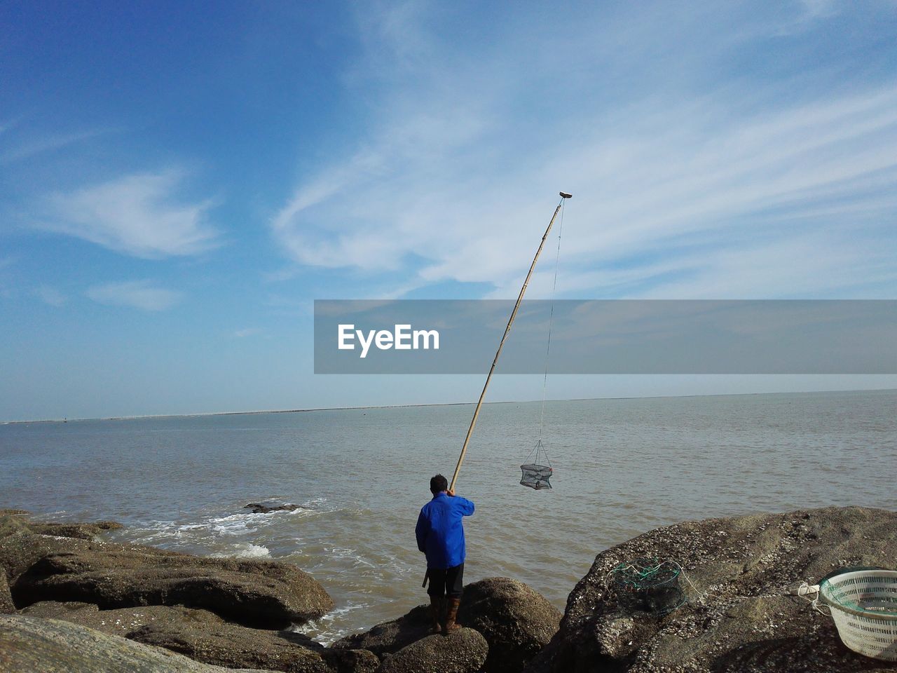 Rear view of man fishing in sea against sky