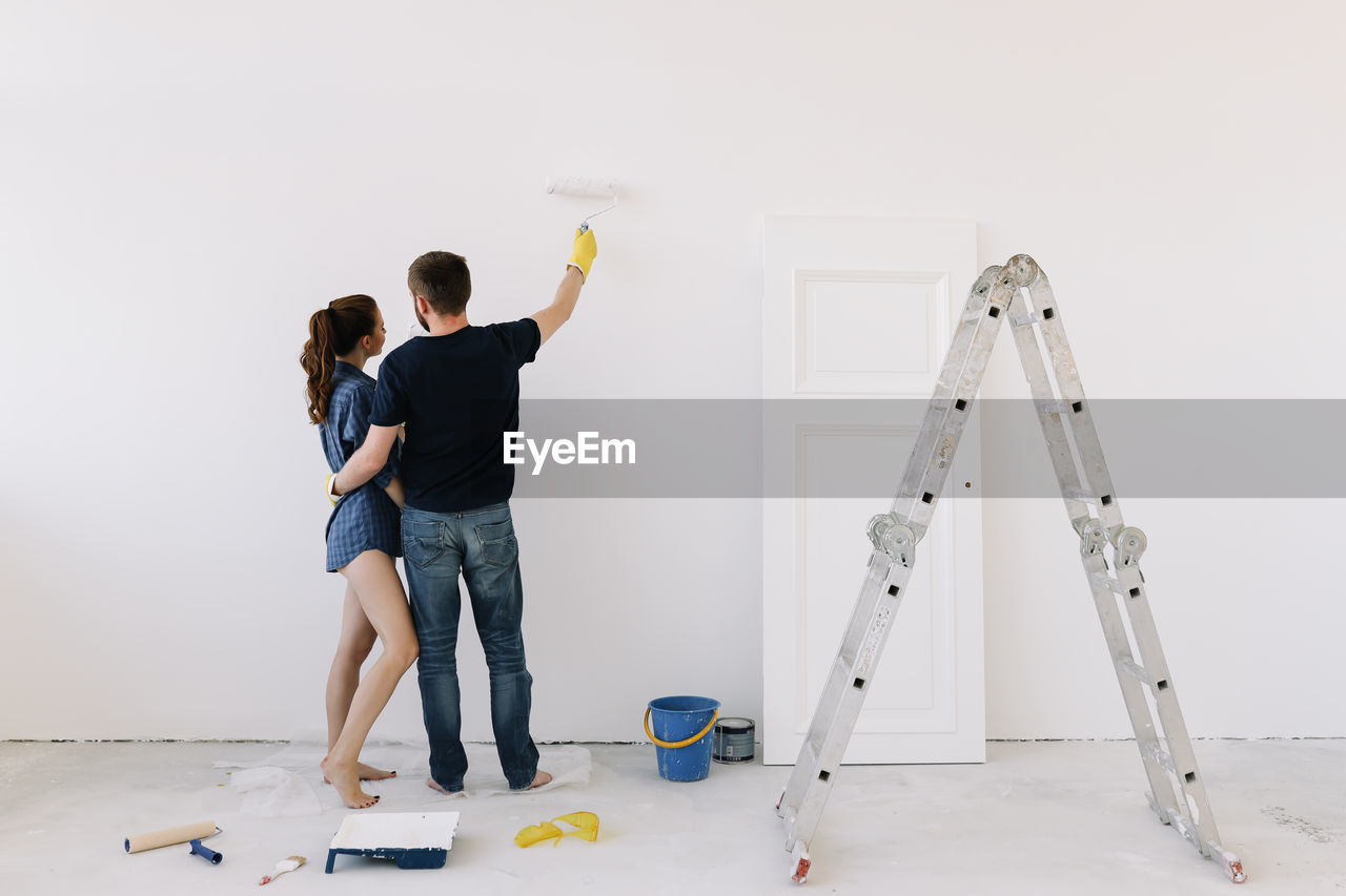 A young couple in love have moved into a new house and are making repairs painting white walls