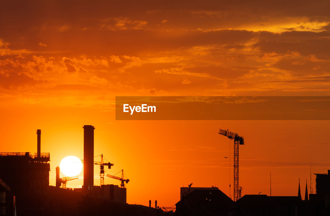 Silhouette of factory against orange sky