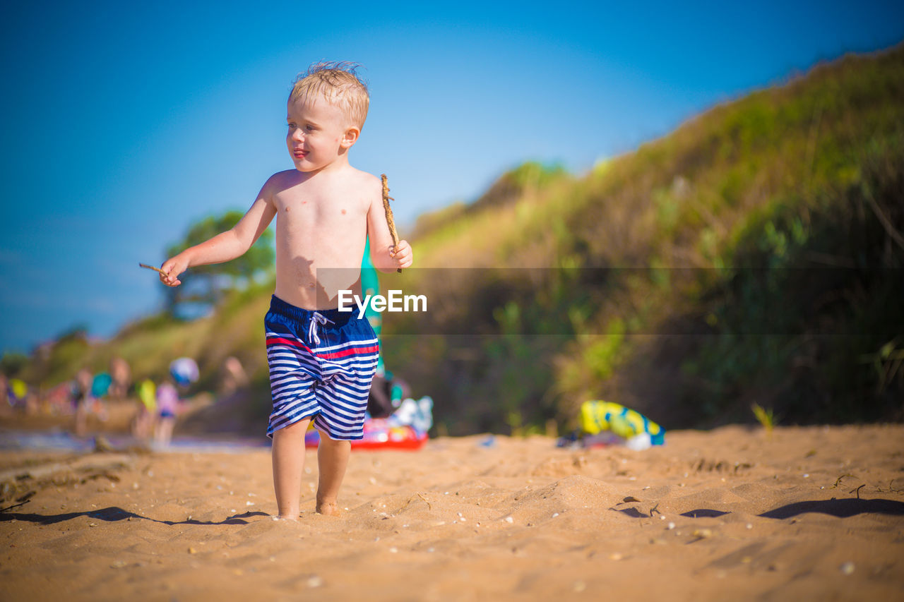 FULL LENGTH OF SHIRTLESS BOY AT BEACH