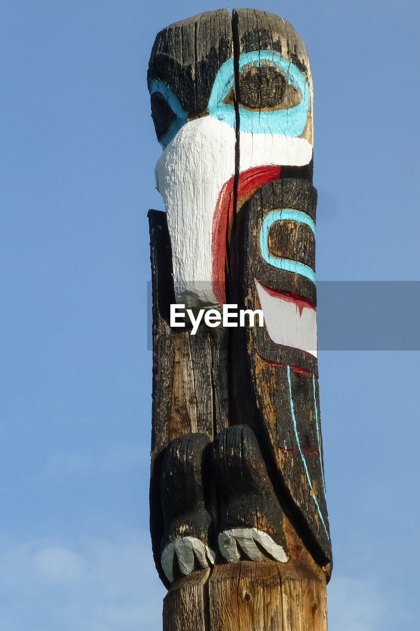 Low angle view of totem pole sculpture against blue sky