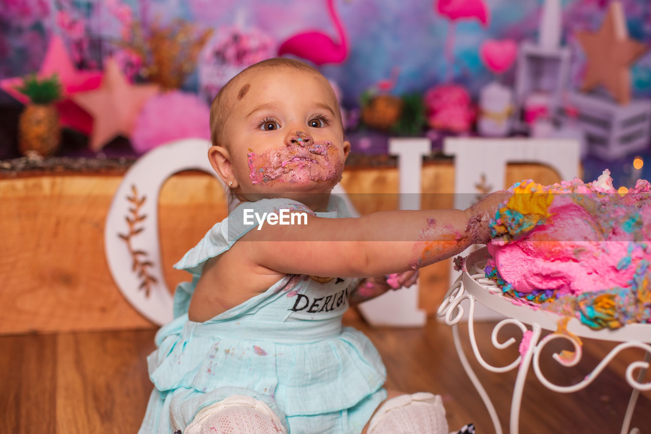 Portrait of cute messy baby girl eating birthday cake