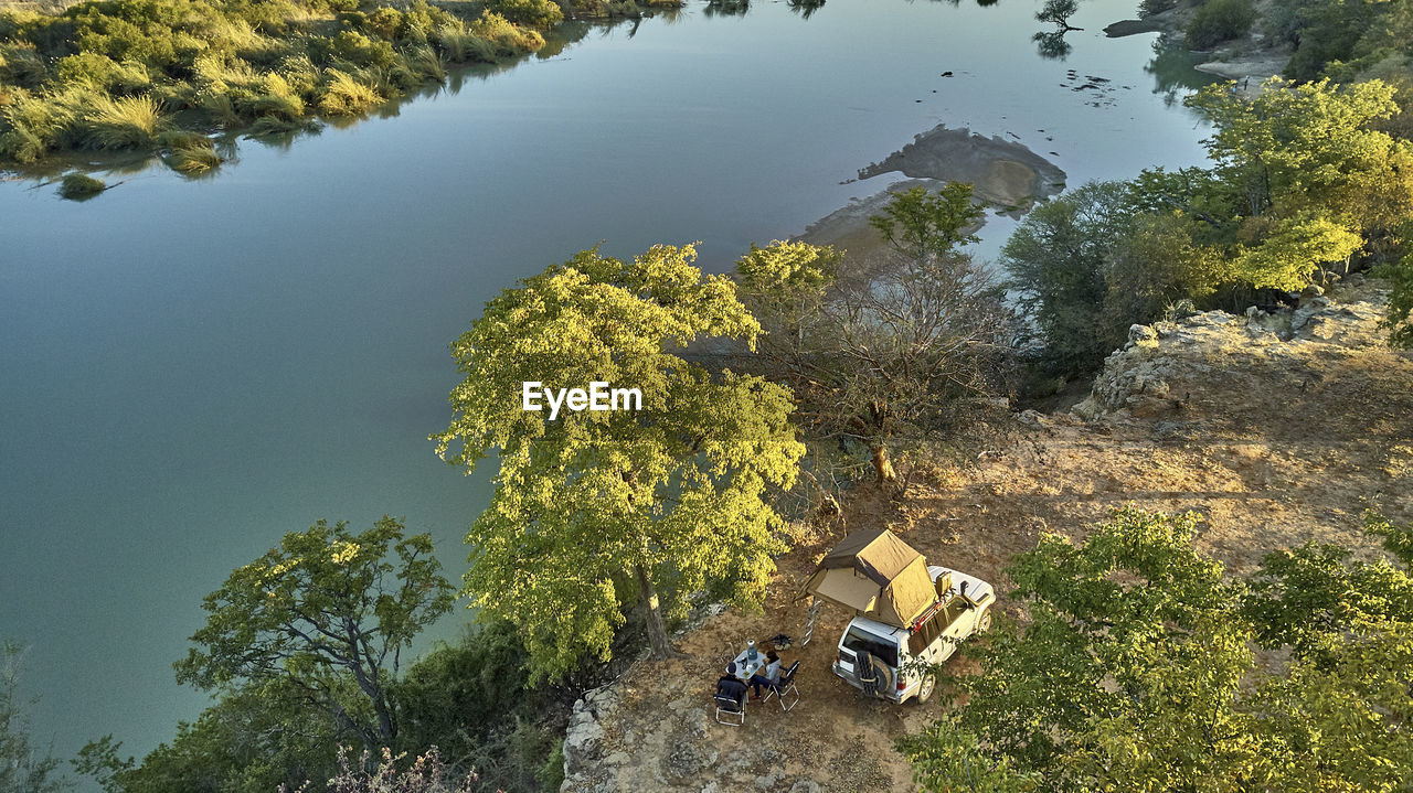 Aerial view of a couple camped with their jeep and rooftop tent and having breakfast in front of the river, cunene river area, angola