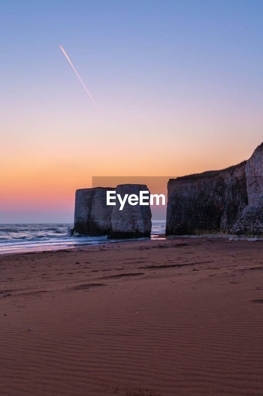 Rocky mountains by sea against clear sky at dusk