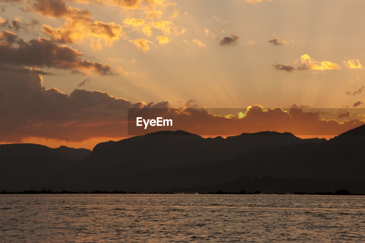 SILHOUETTE MOUNTAINS BY SEA AGAINST SKY DURING SUNSET