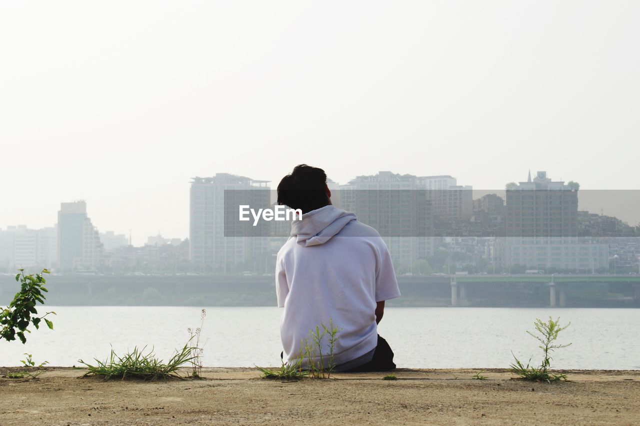 Rear view of man looking at city buildings against clear sky
