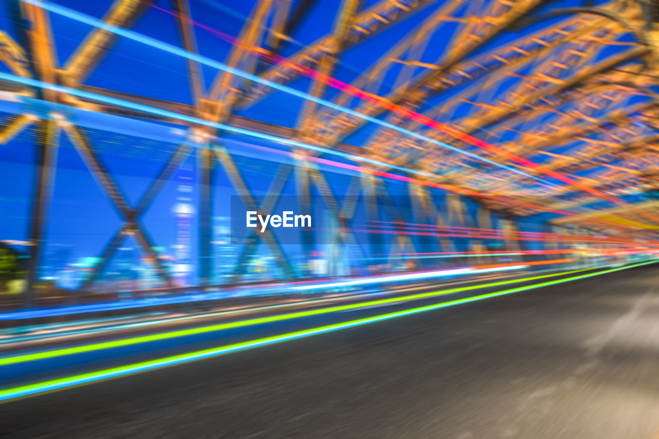 LIGHT TRAILS ON ROAD IN ILLUMINATED CITY