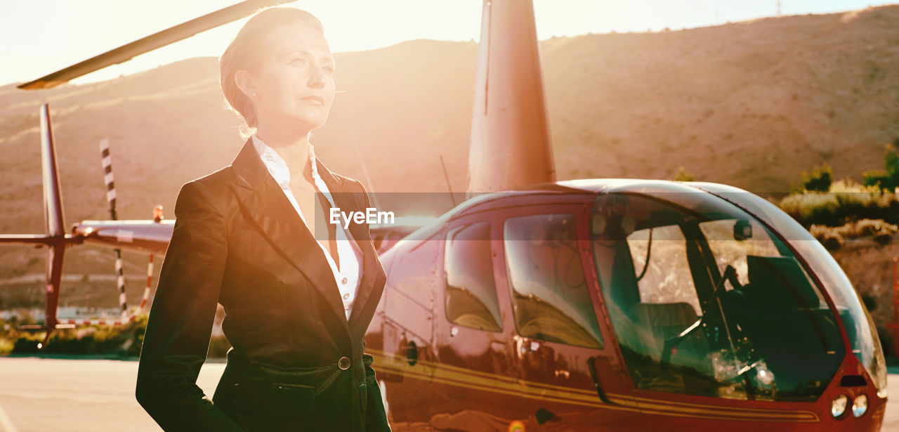 Businesswoman looking away while standing by helicopter during sunny day