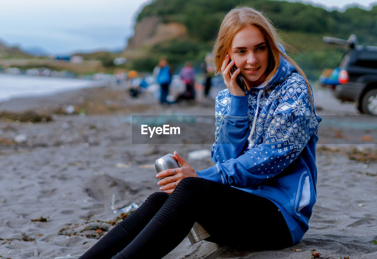 Young woman talking on mobile phone while sitting at beach