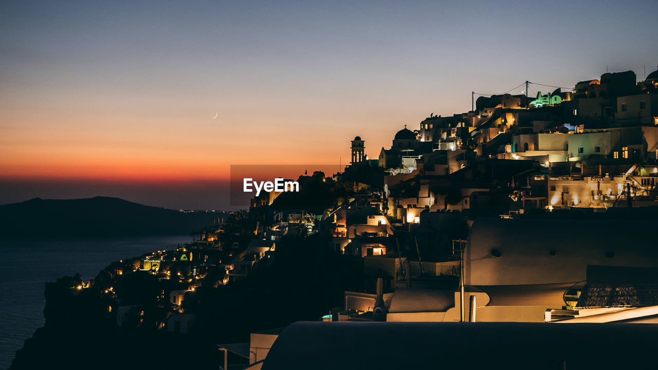 Illuminated townscape by sea against sky during sunset