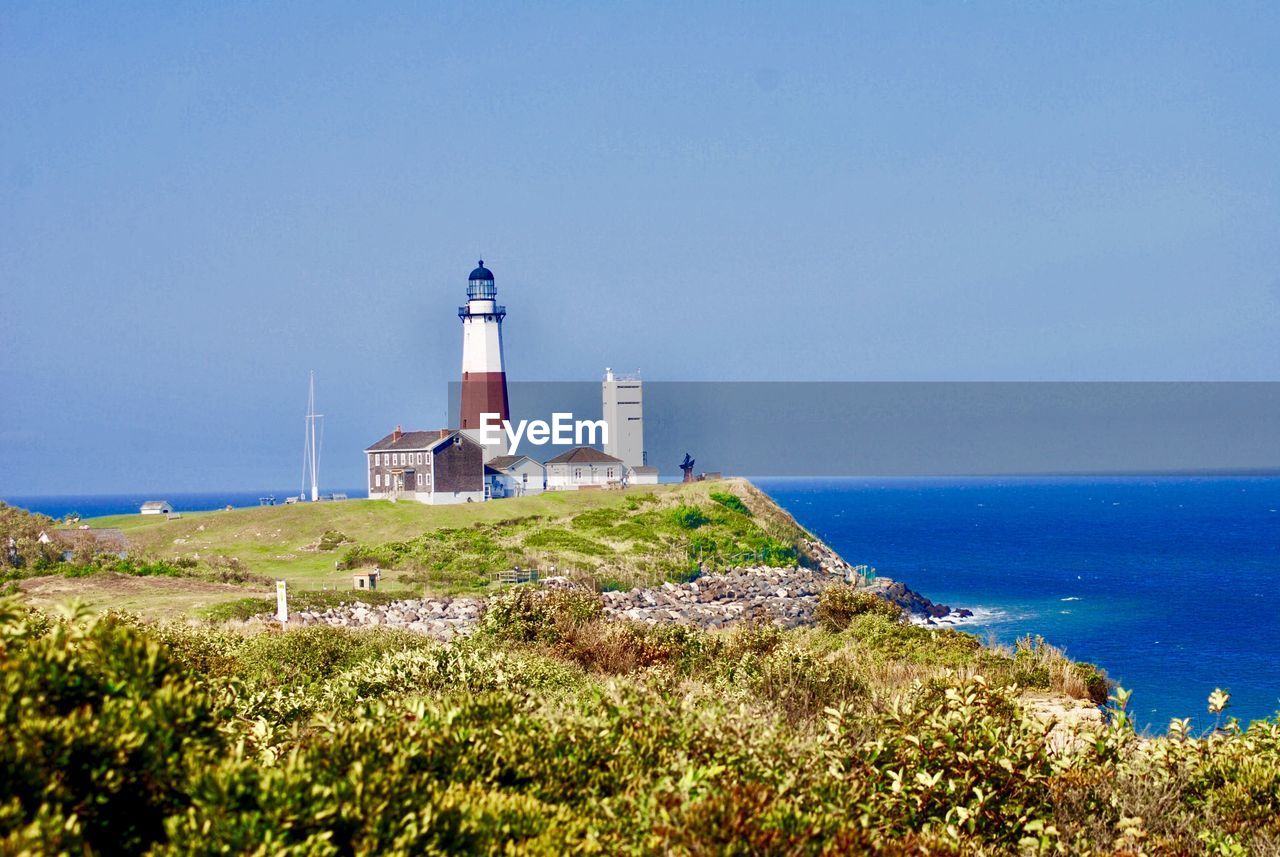LIGHTHOUSE BY SEA AGAINST BUILDINGS