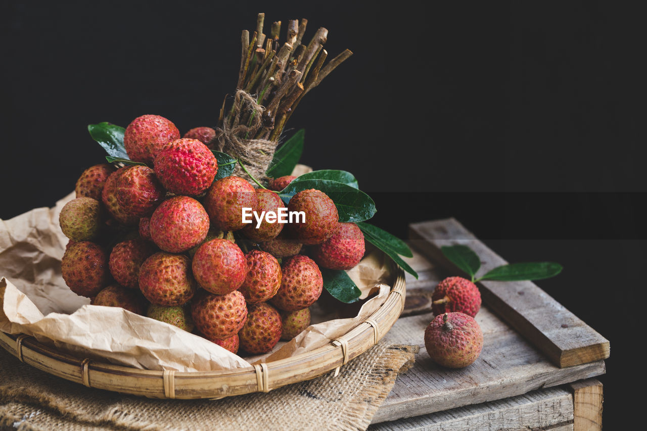 Close-up of lychees in basket on crate against black background