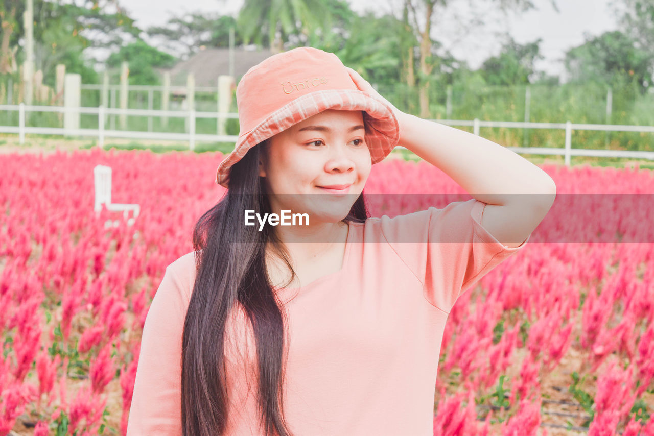 pink, one person, plant, women, flower, flowering plant, adult, hat, smiling, nature, portrait, young adult, spring, happiness, sun hat, clothing, emotion, beauty in nature, long hair, red, waist up, summer, day, lifestyles, hairstyle, standing, leisure activity, outdoors, front view, freshness, field, casual clothing, growth, fashion accessory, female, rural scene, enjoyment, cheerful, landscape, springtime, looking, brown hair, straw hat, agriculture, relaxation, looking at camera, person, grass, child, focus on foreground, teeth