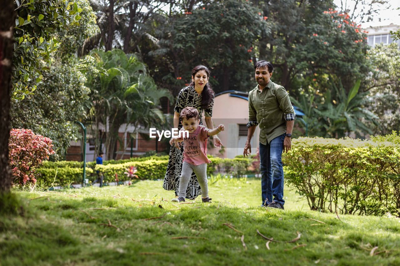 Parents looking at cute son running on grassy land in park