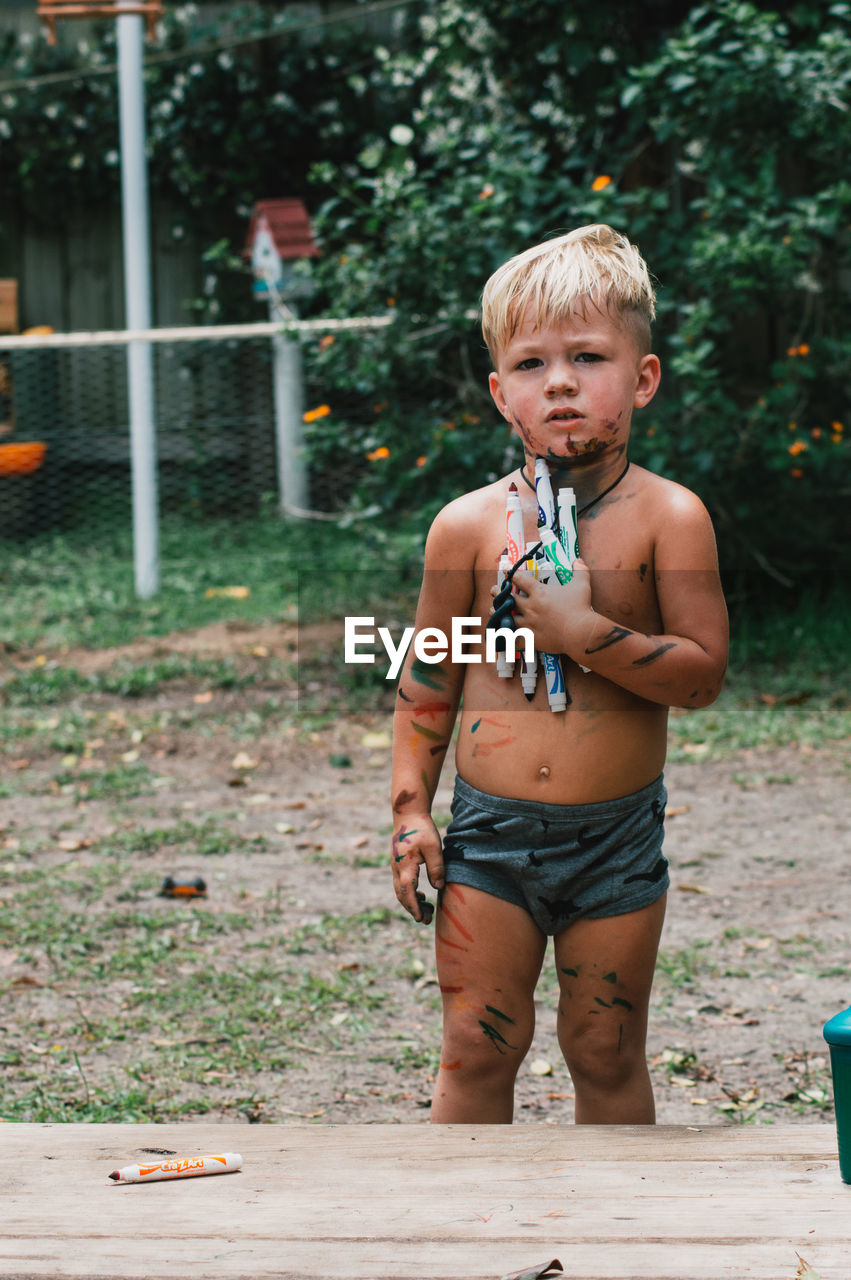 Portrait of shirtless boy standing outdoors with markers.