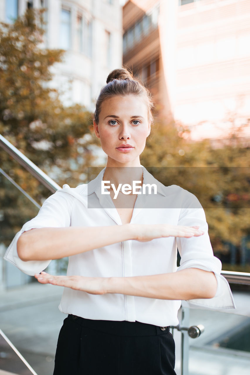 Portrait of young woman gesturing equality sign while standing in city