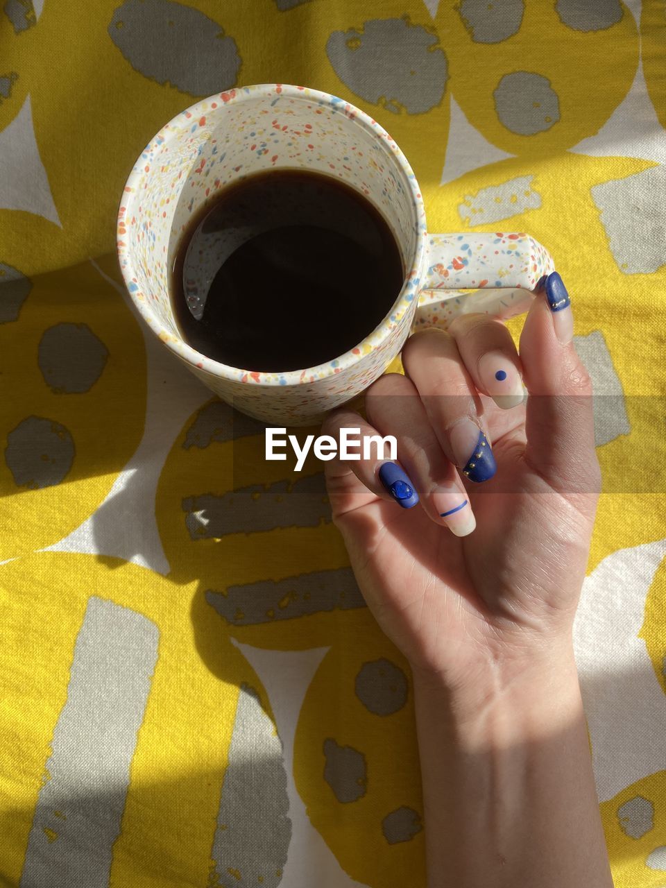 yellow, hand, one person, art, adult, pattern, women, nail polish, cup, nail, high angle view, mug, lifestyles, holding, indoors, coffee cup, creativity, close-up, blue, finger, coffee