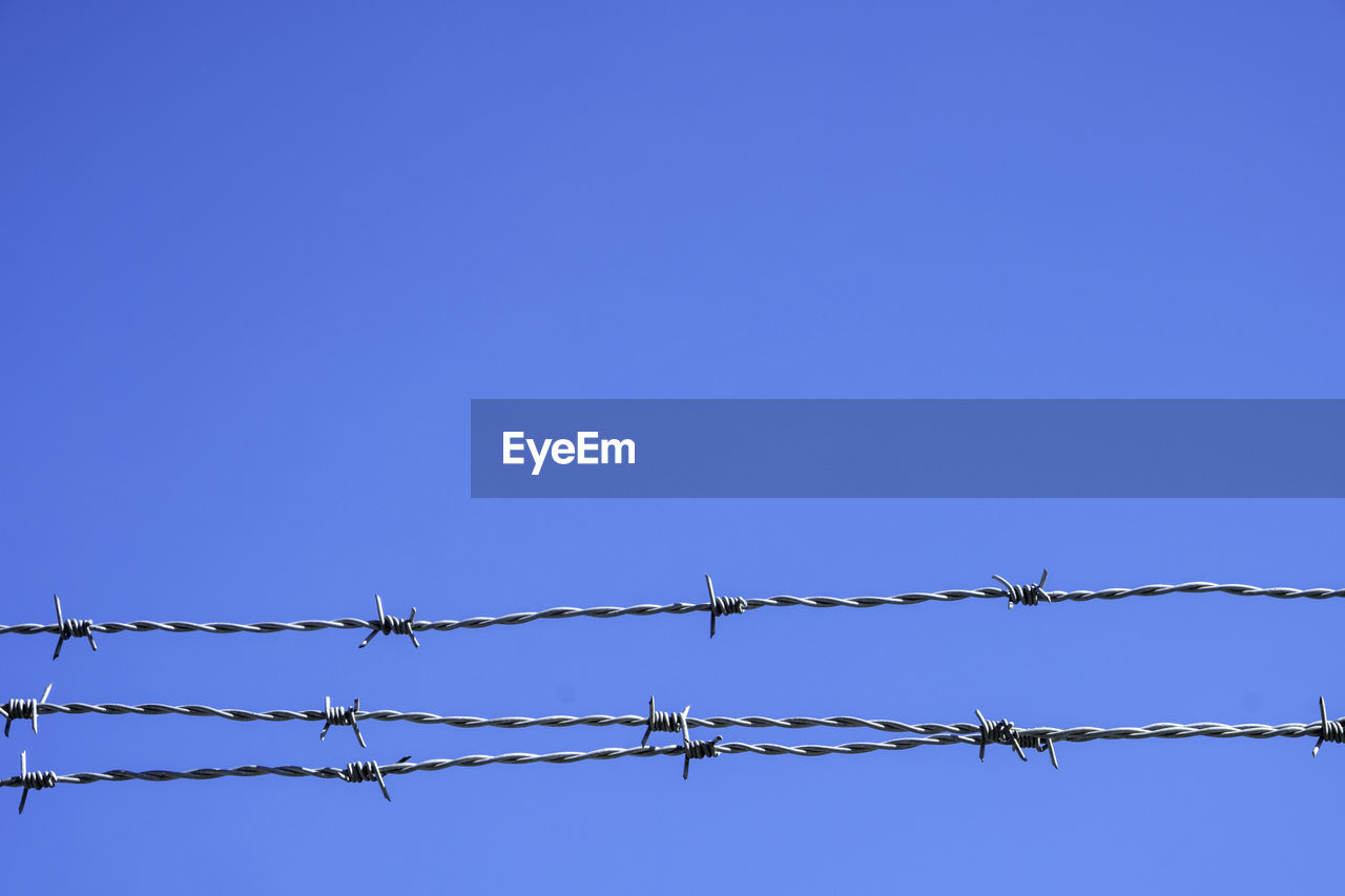 LOW ANGLE VIEW OF BARBED WIRE FENCE AGAINST CLEAR SKY